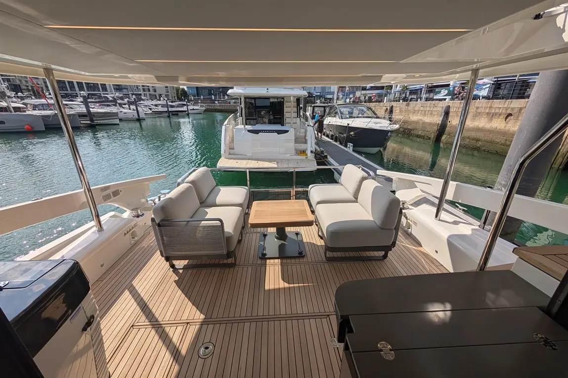 A luxury yacht deck features modern seating with a table, overlooking a marina filled with boats and calm water.